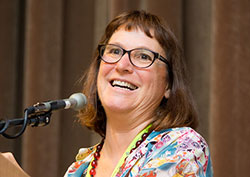 Beth smiling behind a podium and microphone